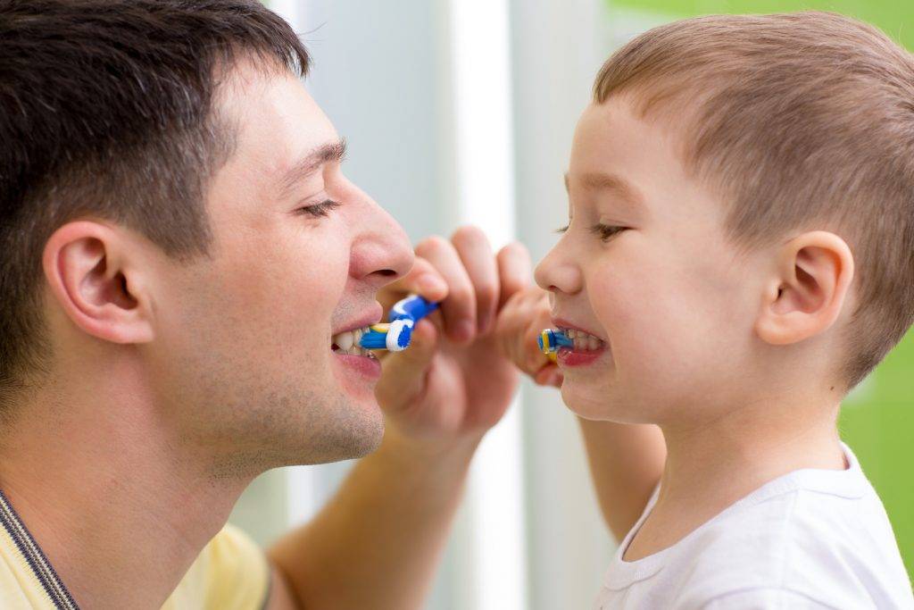 child and his dad brushing teeth in bathroom
