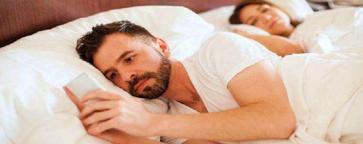 young man texting lover while wife is asleep