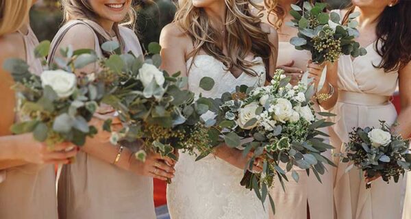 La novia y las damas de honor con ramos de flores en colores pastel se paran una al lado de la otra