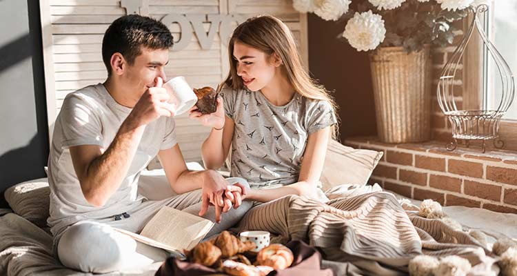 Couple sitting on bed holding each other's hand having breakfast together