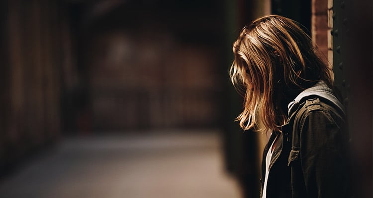 Mujer recostada contra la pared mirando hacia abajo en un pasillo