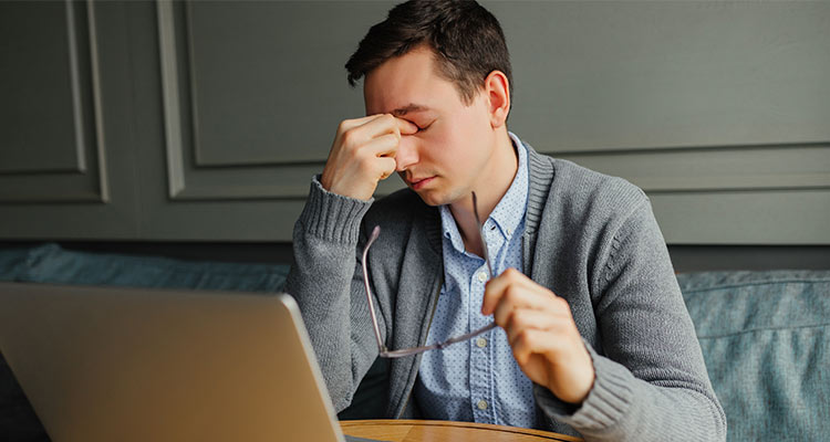 Frustrated young man massaging his nose and keeping eyes closed while working