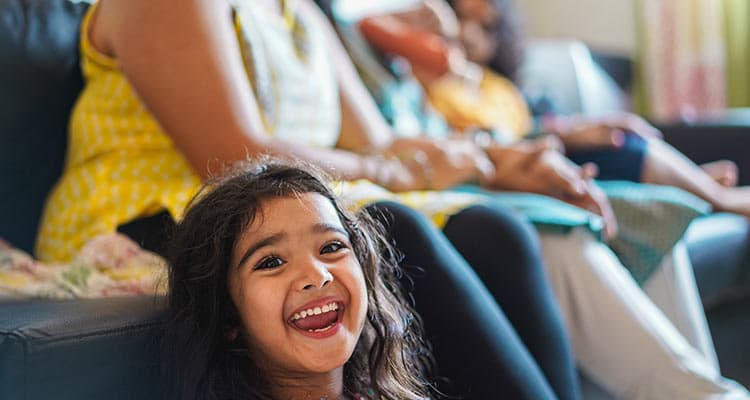 Happy indian girl child wearing sari dress sitting on sofa with parents at home