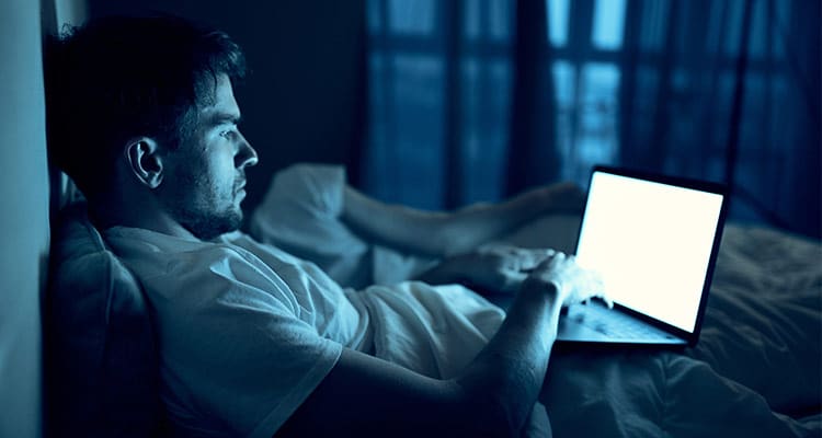 A man works on a laptop in bed, a beloved woman sleeps