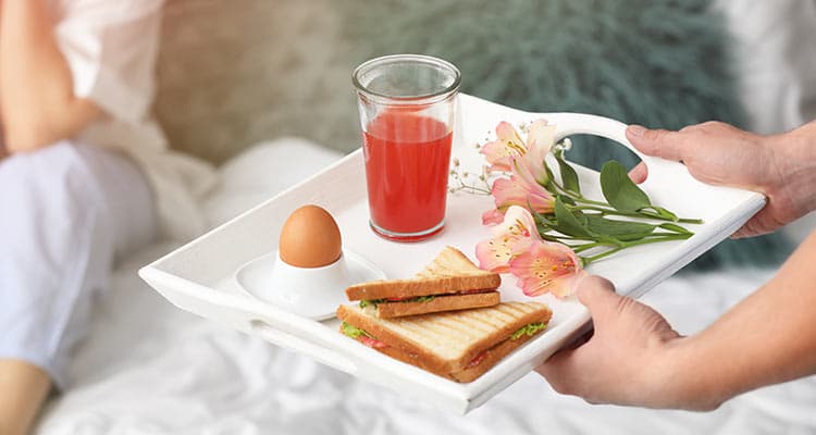 Young woman receiving breakfast in bed from her beloved husband